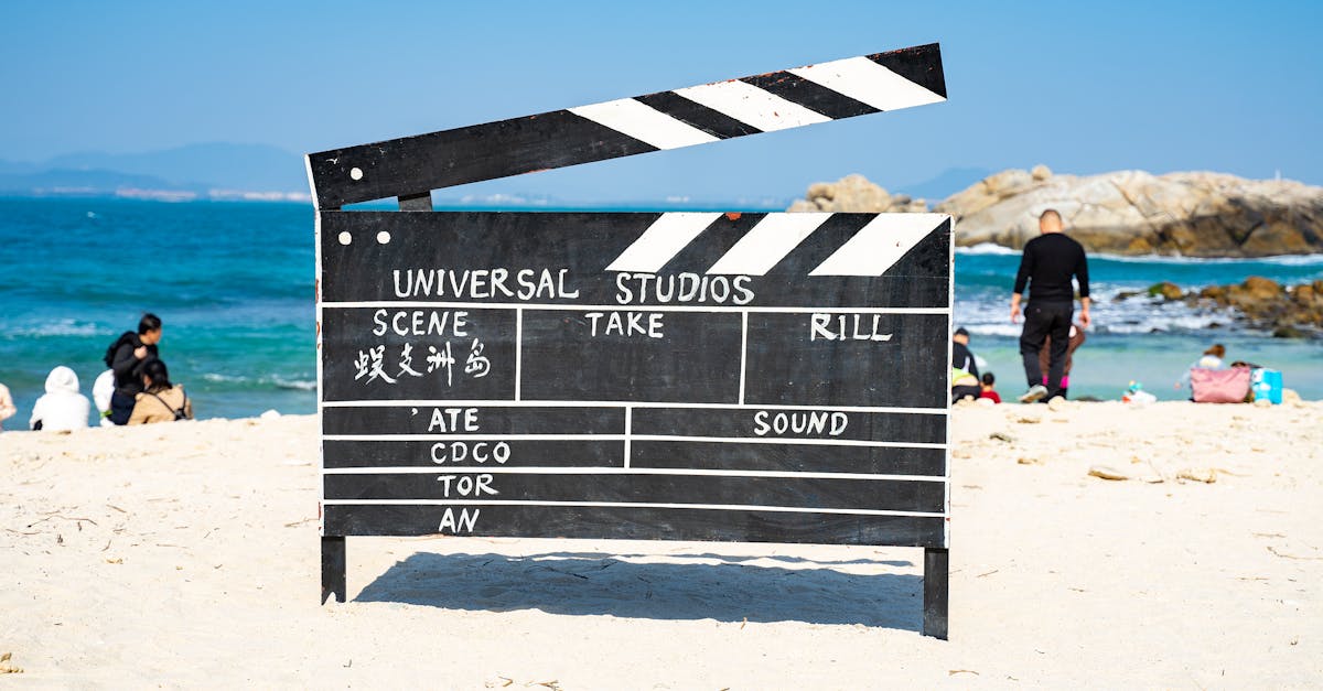 pexels-photo-10739647-10739647 Large film clapperboard on a sandy beach with people and the ocean in the background.