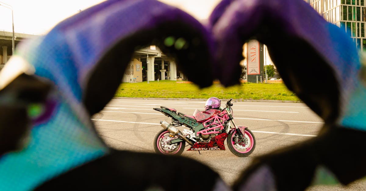 pexels-photo-9606852-9606852 Vibrant pink motorcycle framed by heart-shaped hand gesture with gloves.